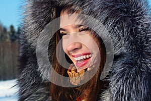 Beautiful girl in fur coat with hood laughs outdoor