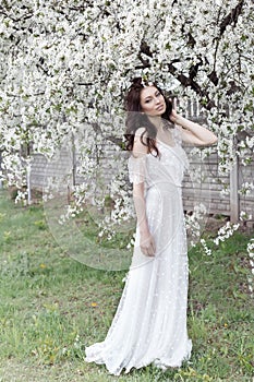 Beautiful girl with gentle make-up long light dress among the flowering trees walks in the spring garden on a warm sun