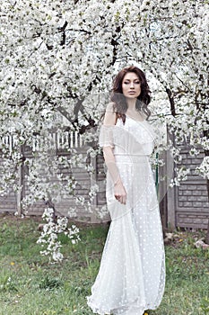 Beautiful girl with gentle make-up long light dress among the flowering trees walks in the spring garden on a warm sun