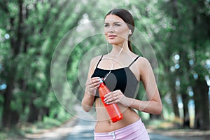 Beautiful girl getting ready for jogging in the park. With thermos bottle in hand.