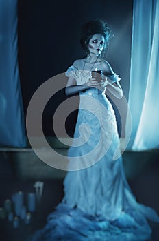 Beautiful girl ghost, witch bride in a white dress holding a black burning candle in hands