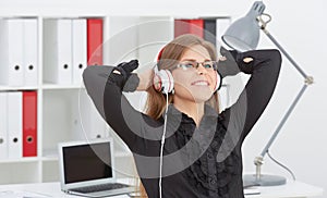 Beautiful girl in glasses with her hands behind her head listening to music on headphones.