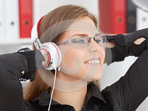 Beautiful girl in glasses with her hands behind her head listening to music on headphones.