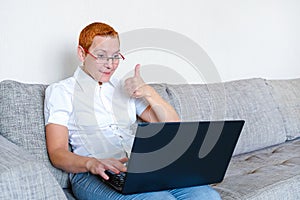A beautiful girl in glasses with a red frame works at the laptop. Emotion of joy with the gesture of a successful transaction