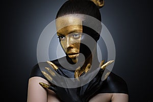 Beautiful girl with gold and black paint on her face and body. Female portrait with creative makeup.way