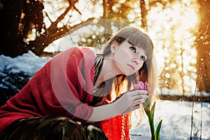 A beautiful girl in a gold dress sits in a spring Sunny forest and touches a Tulip