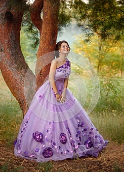 Beautiful girl in a gorgeous purple dress standing under a tree