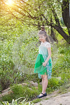Beautiful girl in a green light dress stands against the background of trees