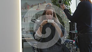 Beautiful girl in the hairdresser drinks coffee. The girl is getting her hair done. Beauty saloon