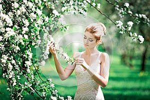Beautiful girl hands with a branch of a blossoming apple tree. Young beautiful blonde woman in blooming garden.