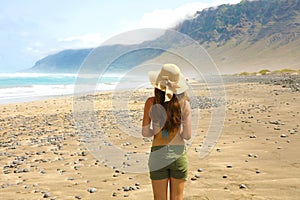 Beautiful girl with hat looking to suggestive landscape of Caleta Famara, Lanzarote, Canary Islands