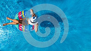 Beautiful girl in hat in swimming pool aerial drone view from above, woman relaxes and swims on inflatable ring donut and has fun