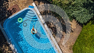 Beautiful girl in hat in swimming pool aerial top view from above, young woman relaxes and swims on inflatable ring donut