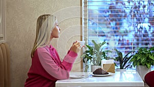 Beautiful girl having breakfast with cappuccino and croissant at a restaurant table near the window. Vertical video