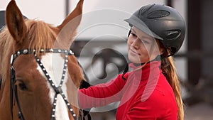 Beautiful girl in helmet stroking a horse outdoors.