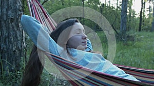 A beautiful girl with her hair loose lies on a hammock. A young woman in a gray jacket is resting on a hammock in the
