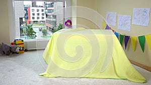 Beautiful girl hide under yellow blanket in children room. 4K