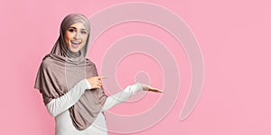 Beautiful girl in hijab pointing at something on her empty palm