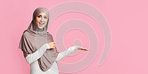 Beautiful girl in hijab pointing at something on her empty palm photo