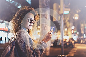 Beautiful girl hipster wearing glasses holding smart phone hands, during night walking in european vocation. Bokeh and