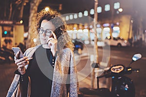 Beautiful girl hipster wearing glasses holding smart phone hands, during night walking in european vocation. Bokeh and