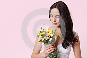 Beautiful girl holding bouquet of flowers isolated on pink background, brunette female looking down on her present, charming lady