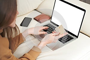 Beautiful girl holding gold credit card in hands and using laptop computer to perform shopping online by inputting card