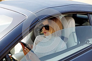 A beautiful girl holding her smartphone in her hands is sitting in the car.