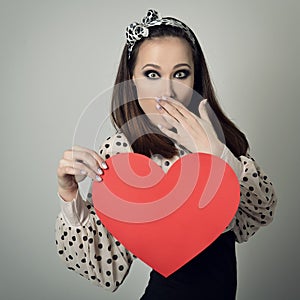 Beautiful girl holding large paper red heart and closing her mouth with hand. Heartbreaker. Temptress. Seductive woman. Portrait photo