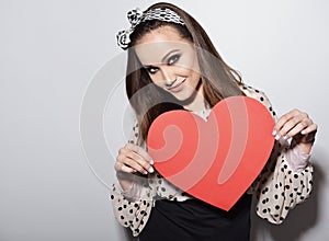 Beautiful girl holding large paper red heart. Heartbreaker. Temptress. Seductive woman. Portrait of funny pinup young fashion photo