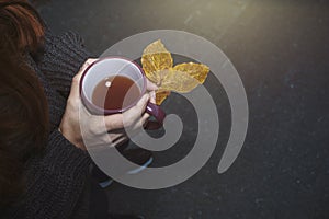 Beautiful girl holding mug of hot tea and leaves in hands. Autumn mood, fall concept