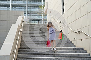 Beautiful girl is holding shopping bags, looking at camera and smiling while walking down the street