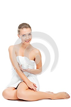 Beautiful girl holding and showing cream for care of skin body. Young woman in towel sitting, on white background