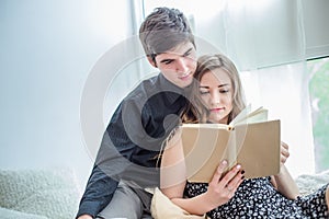 beautiful girl holds a book. guy in love hugs girl and lies on couch