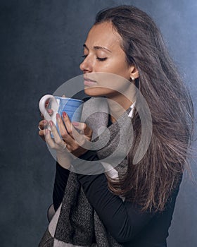 A beautiful girl holds a cup in her hands as the wind blows her long dark brown hair