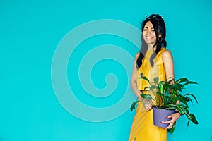 Beautiful girl holds flower in pot on a blue background. Woman hold potted plants. Charming cheerful pin up girl with flower in