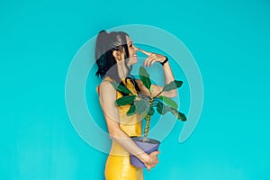 Beautiful girl holds flower in pot on a blue background. Woman hold potted plants. Charming cheerful pin up girl with flower in