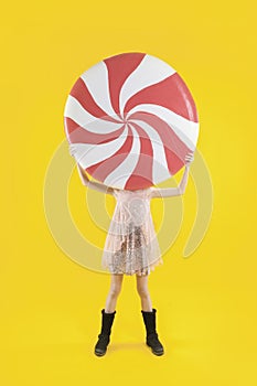 A beautiful girl holds a huge red and white candy in her hands. Lollipop. Sweets for christmas.