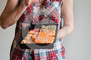A beautiful girl holds Japanese sushi rolls in her hands. Set of sushi rolls with fish. Delivery of ready food home