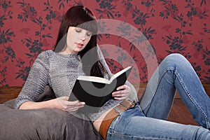 Beautiful girl at home on bean bag reading a book