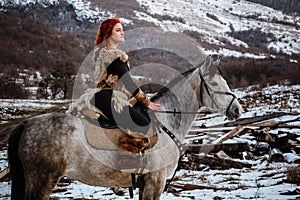 Beautiful girl on horse and with red hair in armor. Woman is a Viking. Fantasy