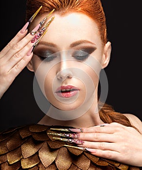 Beautiful girl in the image of the Phoenix with bright makeup, long fingernails and red hair. Beauty face.