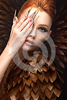 Beautiful girl in the image of the Phoenix with bright makeup, long fingernails and red hair. Beauty face.