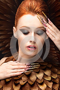 Beautiful girl in the image of the Phoenix with bright makeup, long fingernails and red hair. Beauty face.