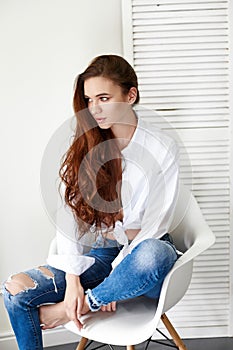 beautiful girl in jeans white shirt sitting on a chair. Gorgeous long hair and charming eyes young woman. Business lady