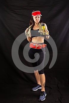 Beautiful girl in jogging red uniform, drinks water after training in the studio on a black background