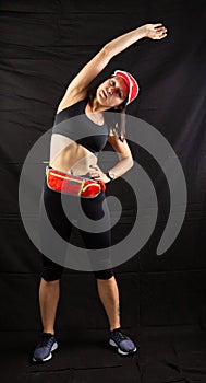 Beautiful girl in a jogging red uniform warming up before training in the studio on a black background