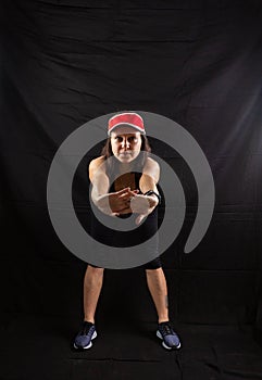 Beautiful girl in a jogging red uniform warming up before training in the studio on a black background