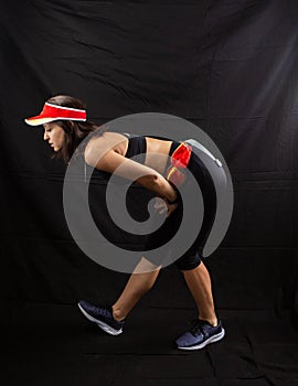 Beautiful girl in a jogging red uniform warming up before training in the studio on a black background