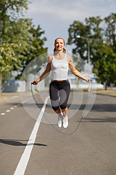 Beautiful girl with a jumping rope. Sports woman jumping on a park background. Active lifestyle concept.